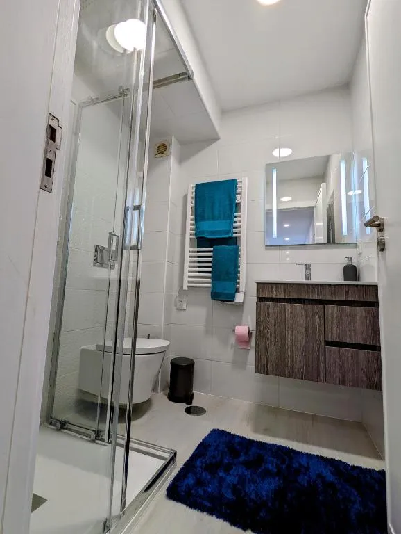 Casa de banho com duche envidraçado, toalheiro aquecido e toalhas azuis